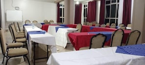 A conference room with multiple tables and chairs, a whiteboard, and red curtains.