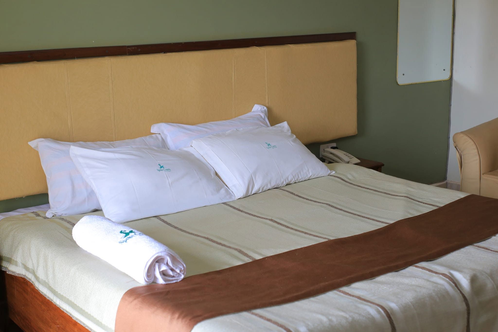 A hotel room with a bed, pillows, a blanket, a telephone, and a chair.