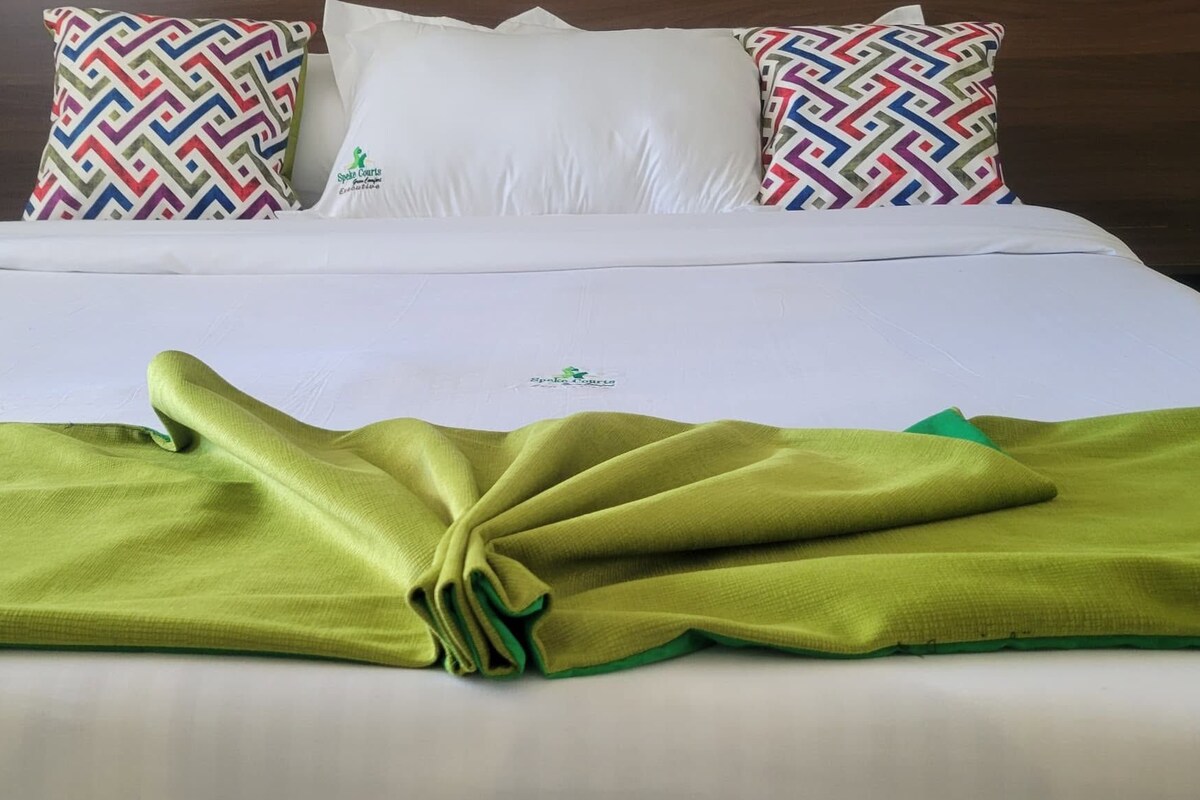 A neatly made bed with a green blanket, white pillows, and a patterned pillow.