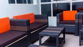 Une pièce meublée avec des meubles en osier, notamment des canapés et une table, agrémentée de coussins orange.
