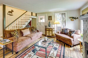 A cozy living room with a staircase, a fireplace, and a bookshelf. - 1/2 Mi to Marina! Lake George Group Getaway (Diamond Point)