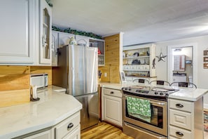 A kitchen with wooden cabinets, a stainless steel refrigerator, a microwave, a stove, and a dining area with chairs. - 1/2 Mi to Marina! Lake George Group Getaway (Diamond Point)