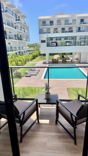 Ein Balkon mit zwei Stühlen, ein Pool und Blick auf ein modernes Gebäude mit mehreren Balkonen.