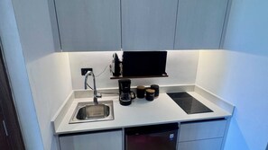 Eine kleine Küchenzeile mit Spüle, einer Kaffeemaschine und einer schwarzen Induktionskochplatte.