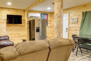 A cozy room with a sofa, a dining table with chairs, a refrigerator, and a television mounted on the wall. - Hunt, Fish & Stargaze: Doniphan Cabin on 25 Acres (Doniphan)