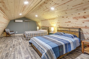 A bedroom with two beds, a bench, a bedside table with a lamp, and an air conditioning unit. - Hunt, Fish & Stargaze: Doniphan Cabin on 25 Acres (Doniphan)