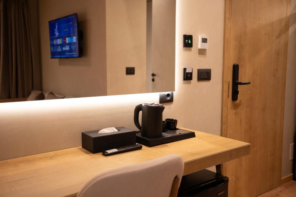 Habitación de hotel con un escritorio de madera, un control remoto, una cafetera y un televisor montado en la pared.
