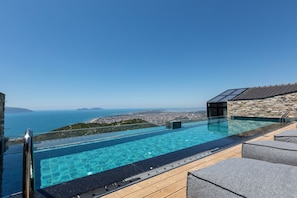 A rooftop infinity pool with a clear view of the sea and cityscape.