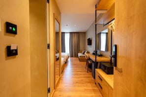 Una habitación de hotel con piso de madera, un escritorio con silla, una cama, un sofá y un televisor montado en la pared.
