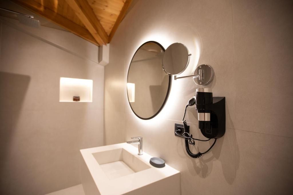 Un baño con un lavamanos blanco, un espejo y un teléfono instalado en la pared.