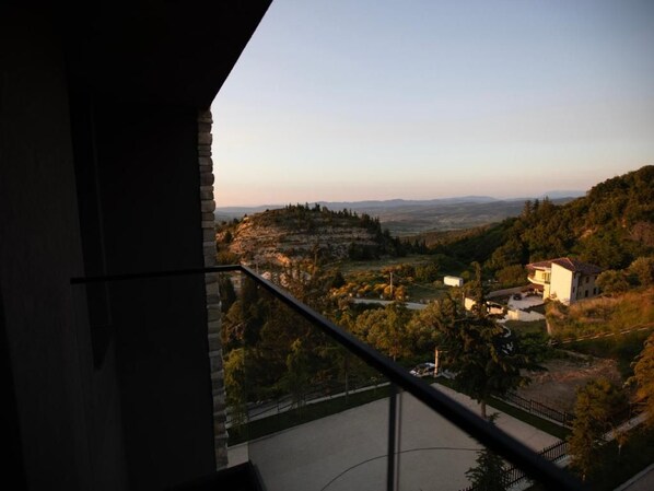 A balcony with a view of a hilly landscape, a building, and a clear sky.