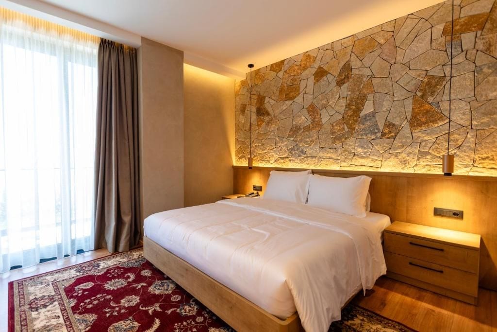 A hotel room with a large bed, a nightstand, a wall-mounted lamp, and a patterned rug.