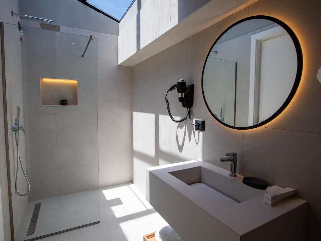 Un baño moderno con ducha de vidrio, un lavabo blanco y un espejo redondo con marco negro.
