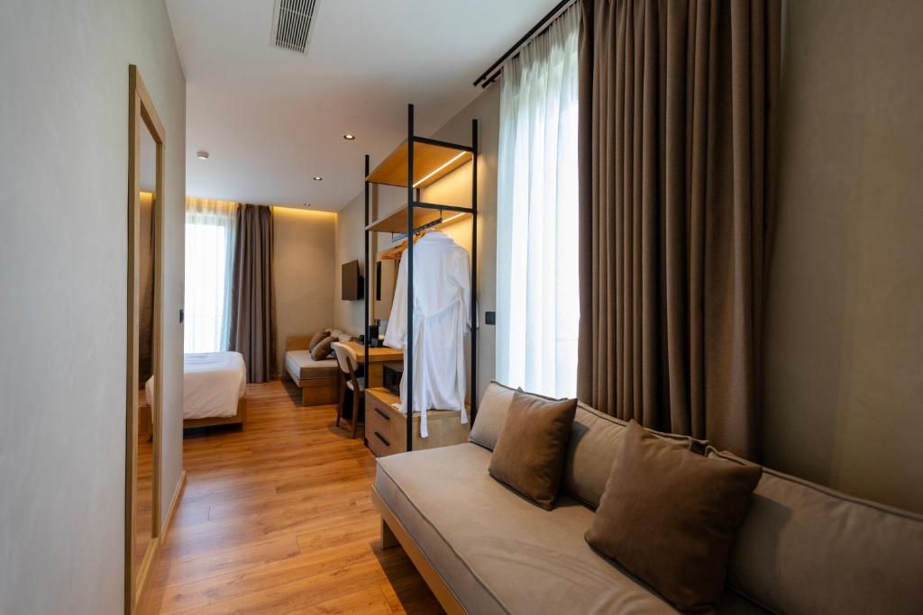 A hotel room with a bed, a sofa, a desk with a chair, a wardrobe, and a mirror.