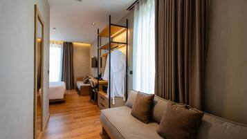 A hotel room with a bed, a sofa, a desk with a chair, a wardrobe, and a mirror.