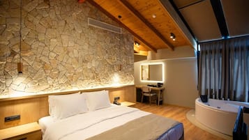 A bedroom with a stone wall, wooden ceiling beams, a bed, a desk, and a bathtub.