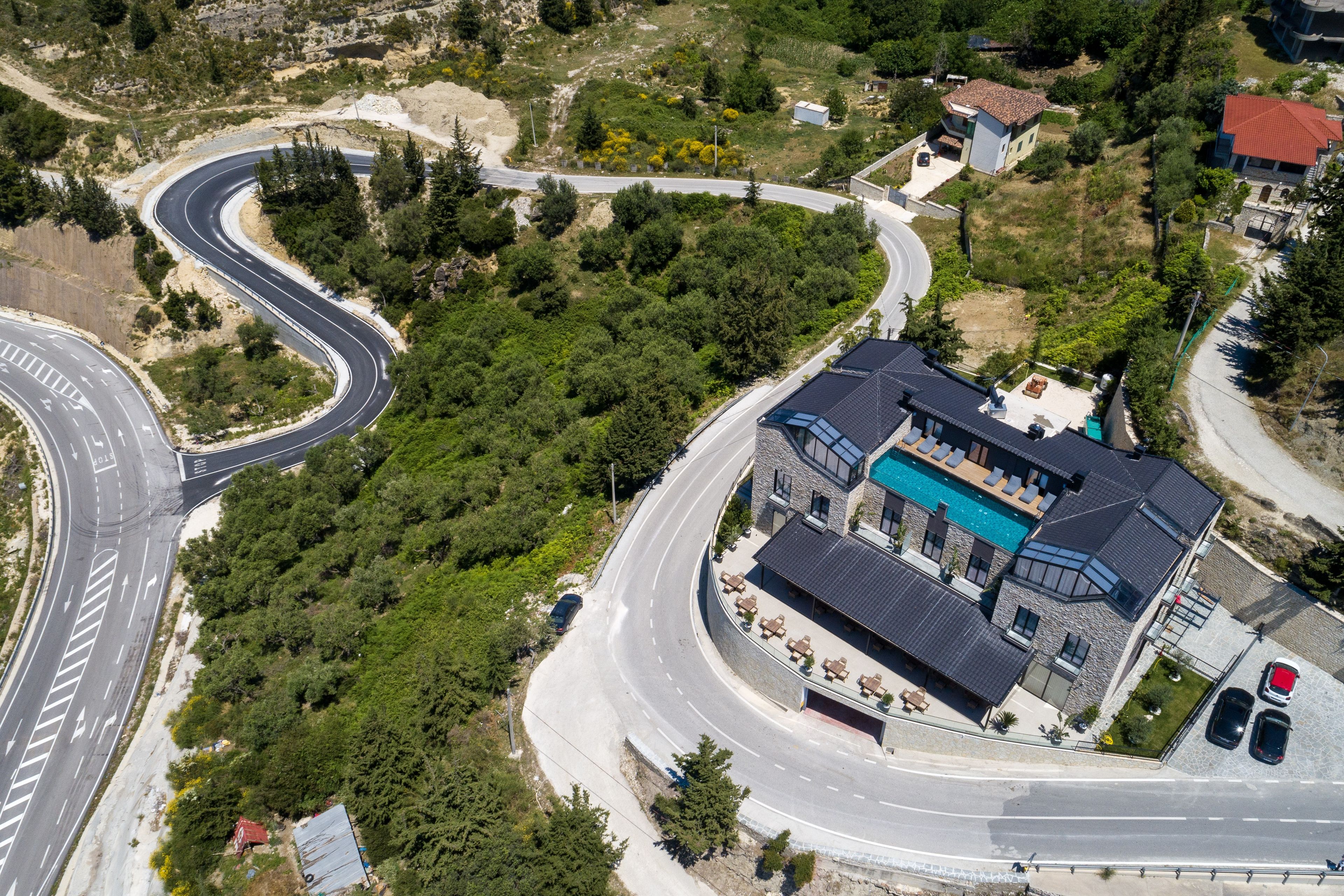 A large building with a swimming pool, surrounded by a winding road and greenery.