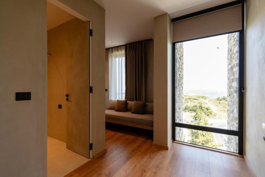 A modern interior with a wooden floor, a sliding glass door leading to a balcony, and a seating area with a sofa and curtains.