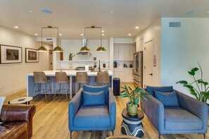 A modern kitchen with a central island, bar stools, pendant lighting, and a dining area with sofas. - Walk to Beach! Condo w/ Shared Rooftop Patio (Oceanside)
