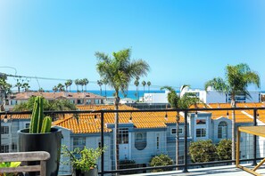 A terrace with a view of a coastal town, featuring buildings with orange tiled roofs and palm trees. - Walk to Beach! Condo w/ Shared Rooftop Patio (Oceanside)