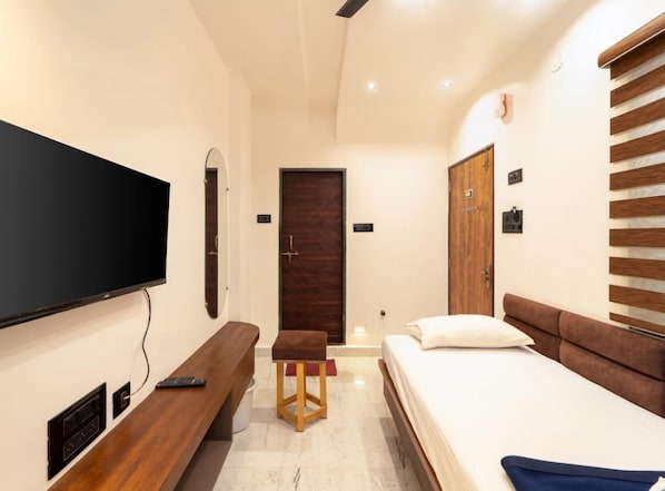 A hotel room with a flat-screen TV mounted on the wall, a wooden bench, a bed with a brown headboard, and a wooden door.