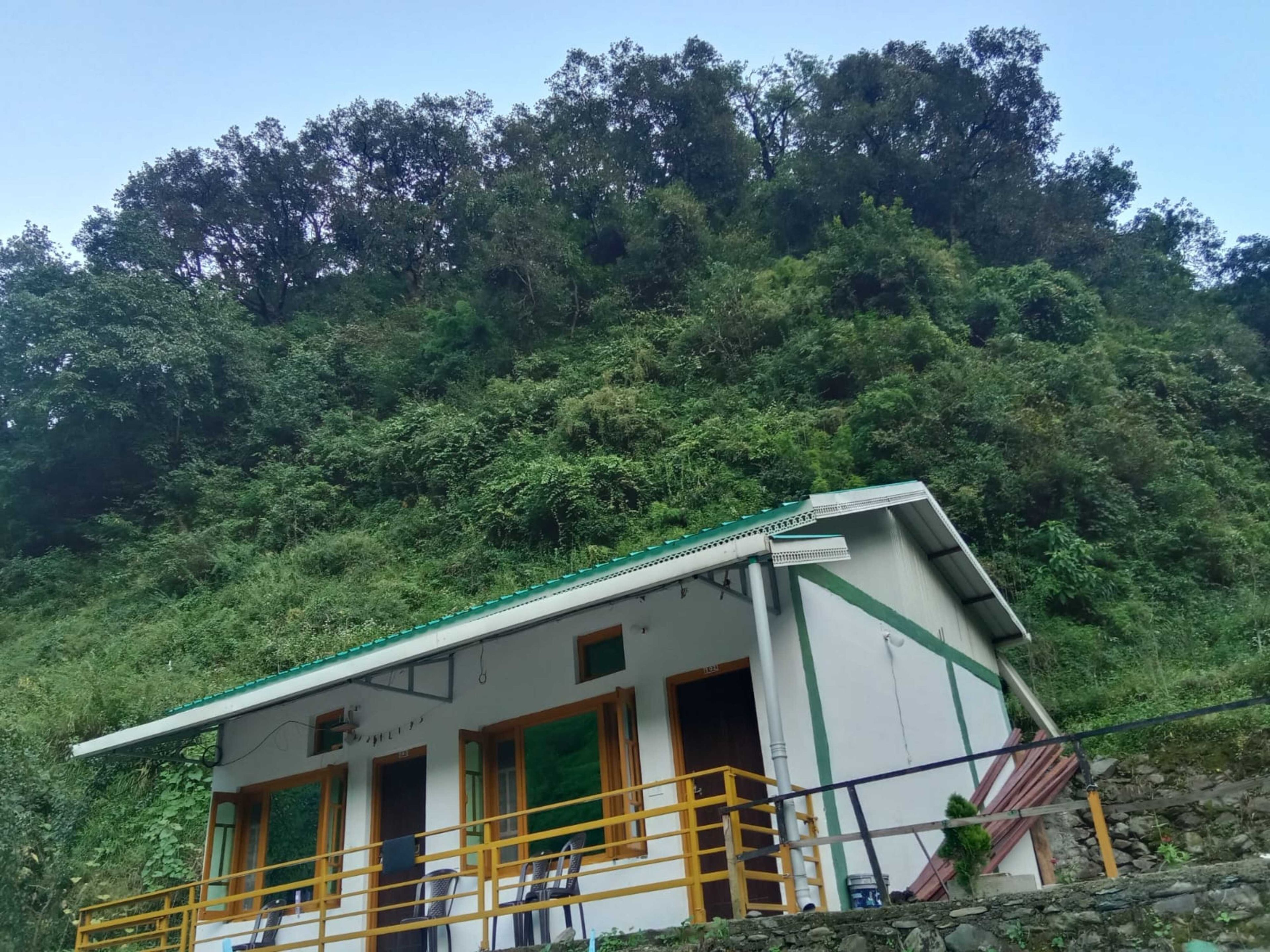 A small building with a green roof, a balcony with yellow railings, and a stone wall in the foreground.