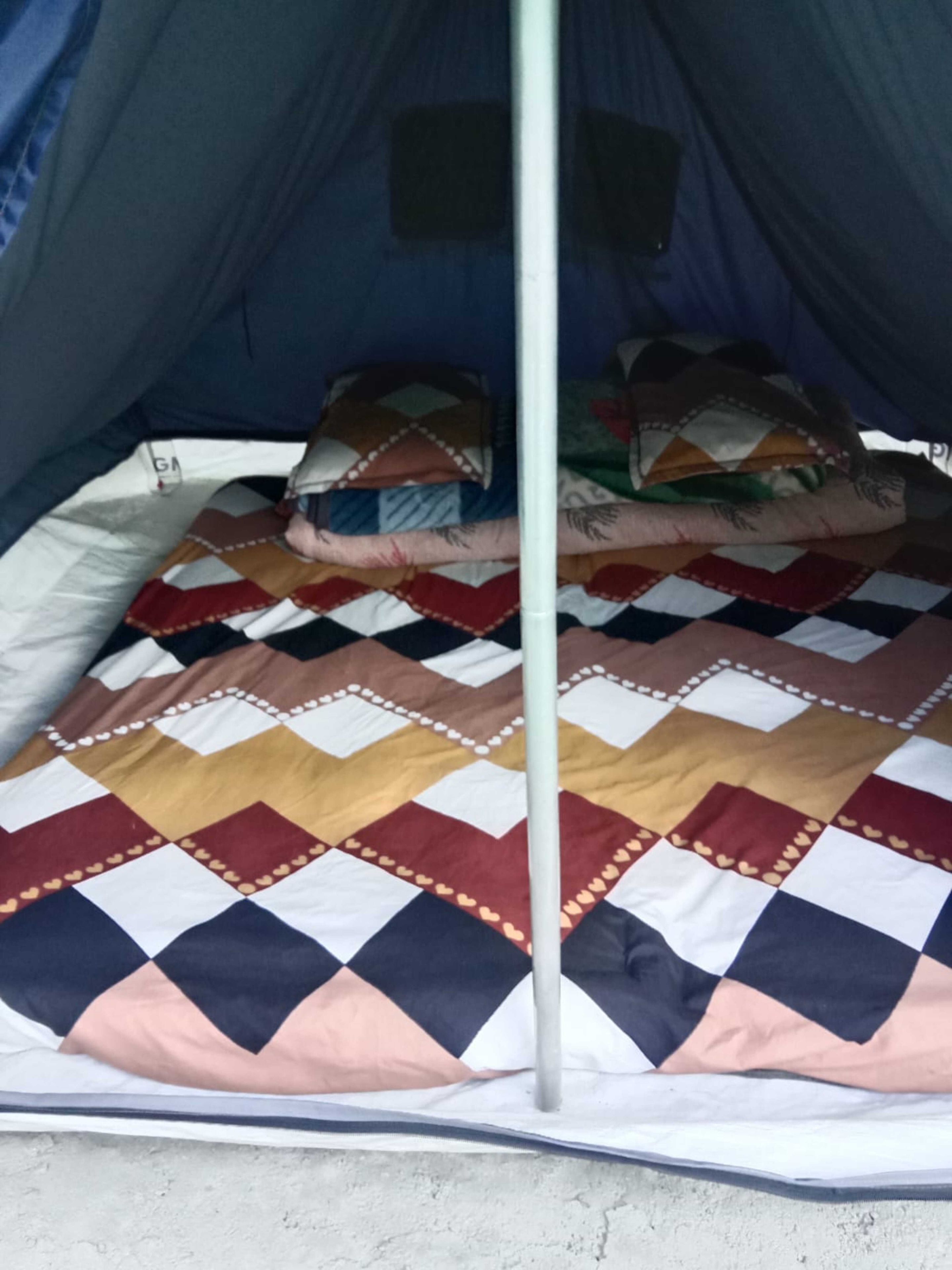 Una carpa con un edredón estampado, un mástil y almohadas.