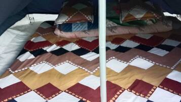 Una carpa con un edredón estampado, un mástil y almohadas.