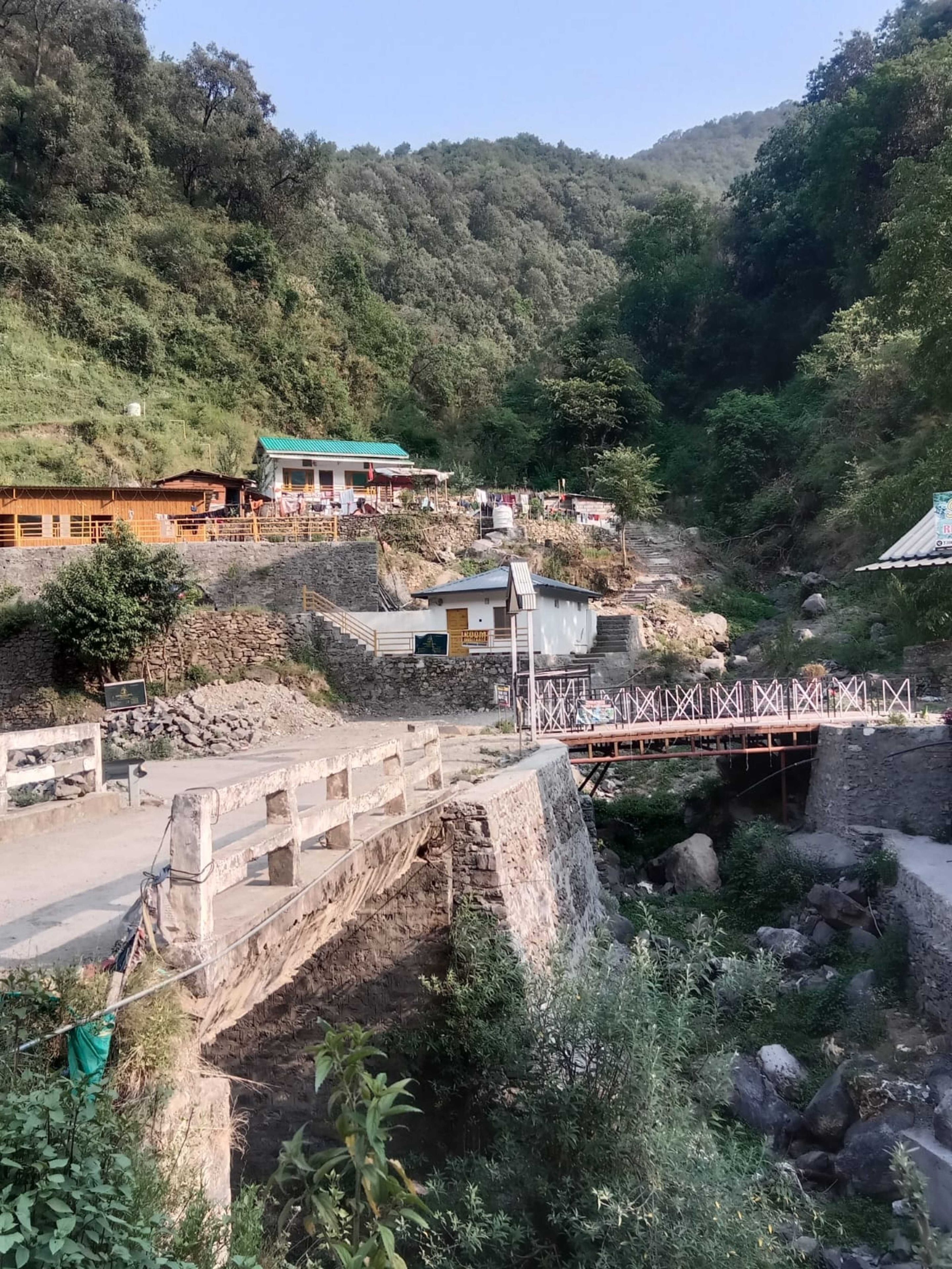 Paisatge rural amb un pont de pedra, edificis de fusta i un turó.