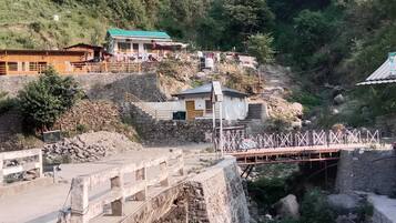 Paisatge rural amb un pont de pedra, edificis de fusta i un turó.