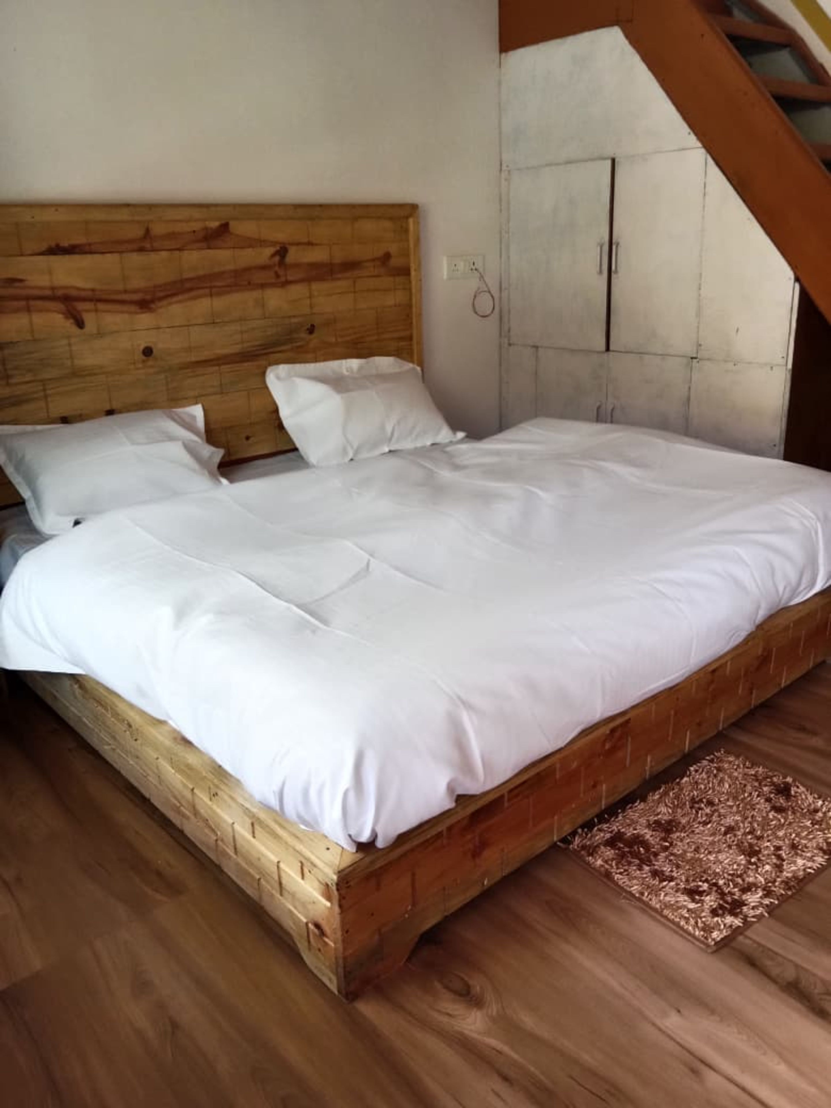 Un lit en bois, avec une literie blanche, dans une pièce dont le sol est recouvert de planches de bois et qui possède un plafond en pente.