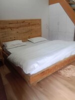 Una cama individual con cabecera de madera y ropa de cama blanca en una habitación con piso de madera.