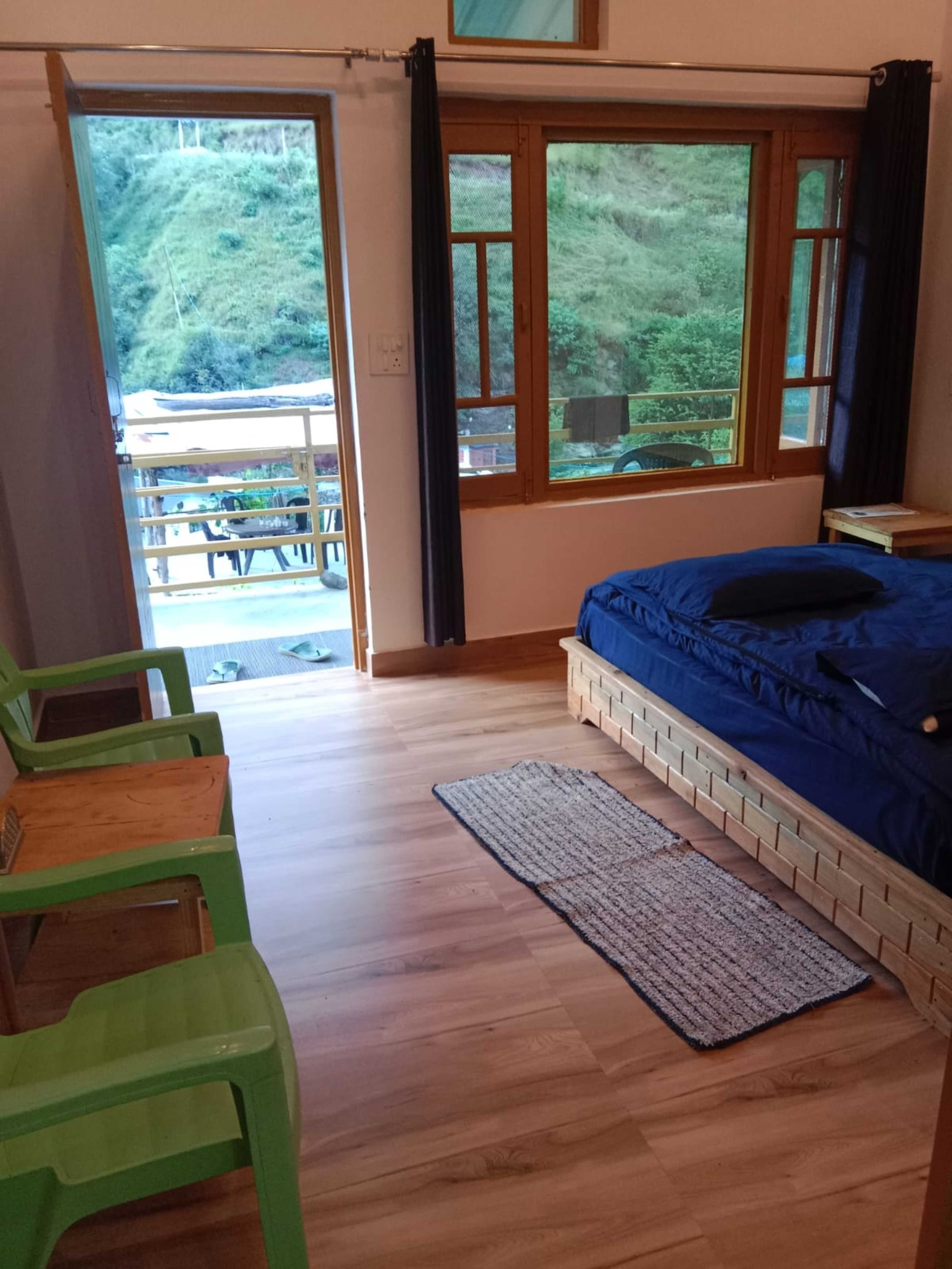 A bedroom with a bed, a wooden floor, a green chair, and a view of a balcony.