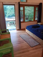 Un dormitorio con cama, piso de madera, una silla verde y vistas a un balcón.