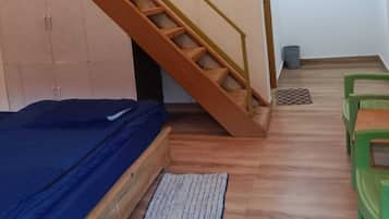 A room with a wooden staircase, a bed, a small table, and green chairs.