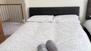 Een opgemaakt bed met een bloemenprint deken en twee opgerolde handdoeken.