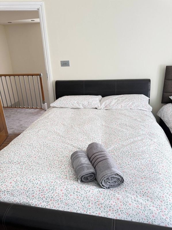 Een opgemaakt bed met een bloemenprint deken en twee opgerolde handdoeken.