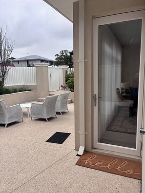 A covered patio area with wicker furniture, a sliding glass door, and a 'hello' mat.