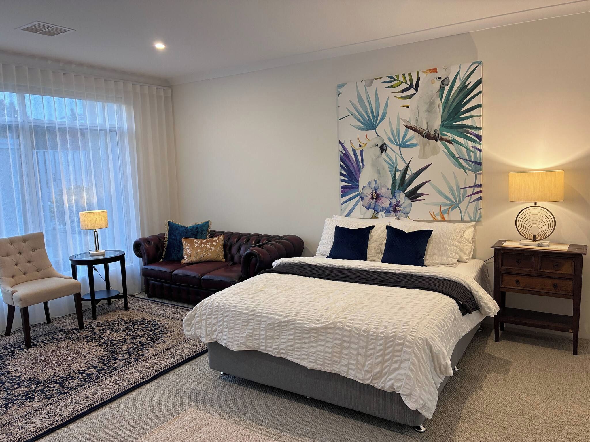 Una habitación de hotel con cama, sofá, sillón, mesita de noche y lámpara.