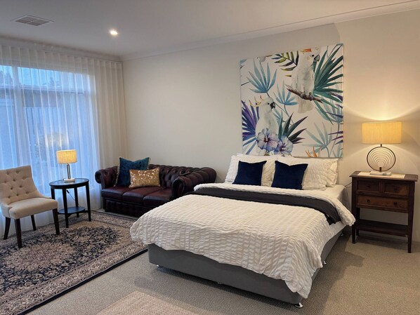 A hotel room with a bed, a sofa, a chair, a nightstand, and a lamp.