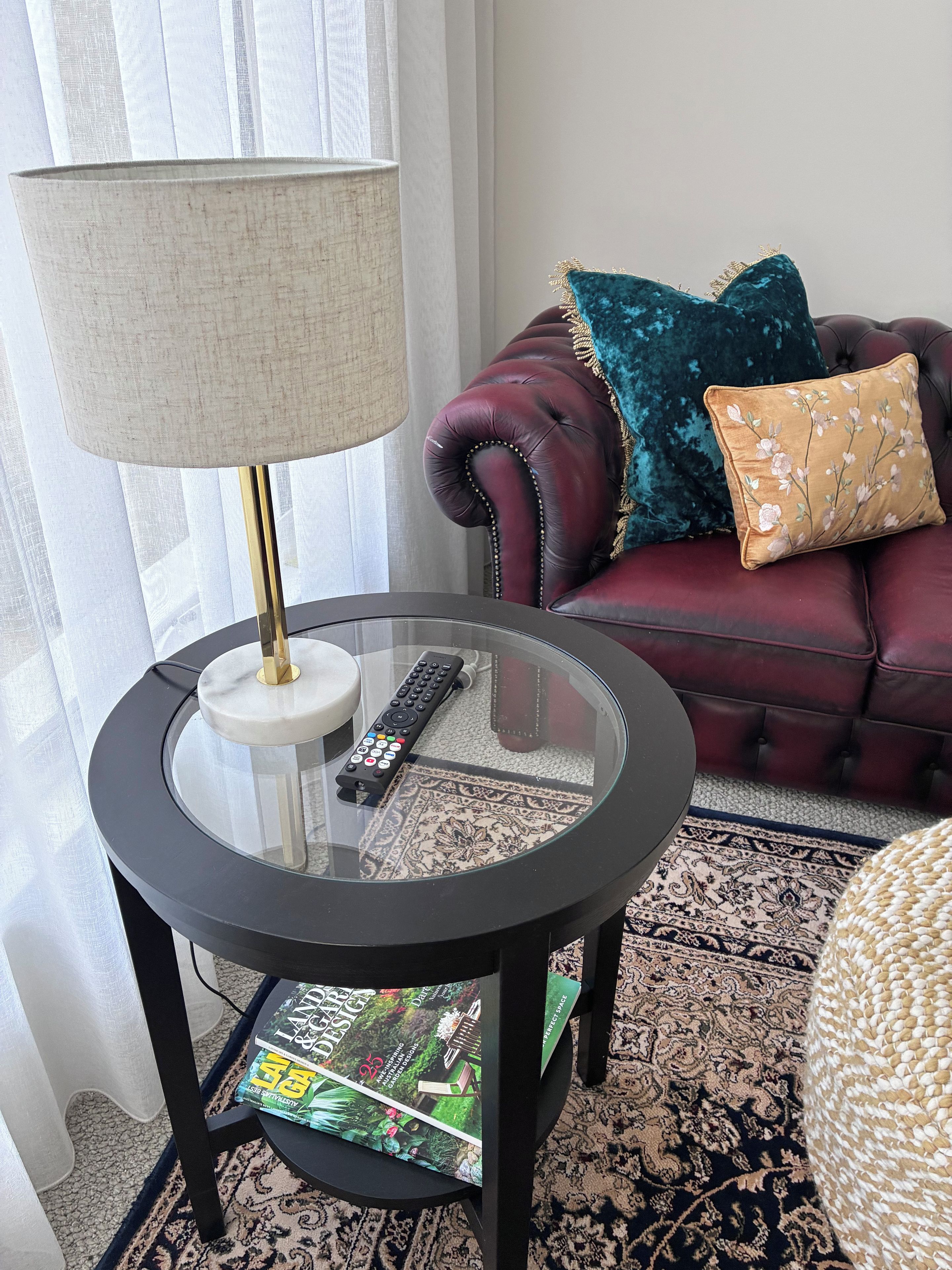 A glass-top table with a remote control, a magazine, and a lamp.
