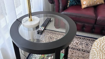 A glass-top table with a remote control, a magazine, and a lamp.