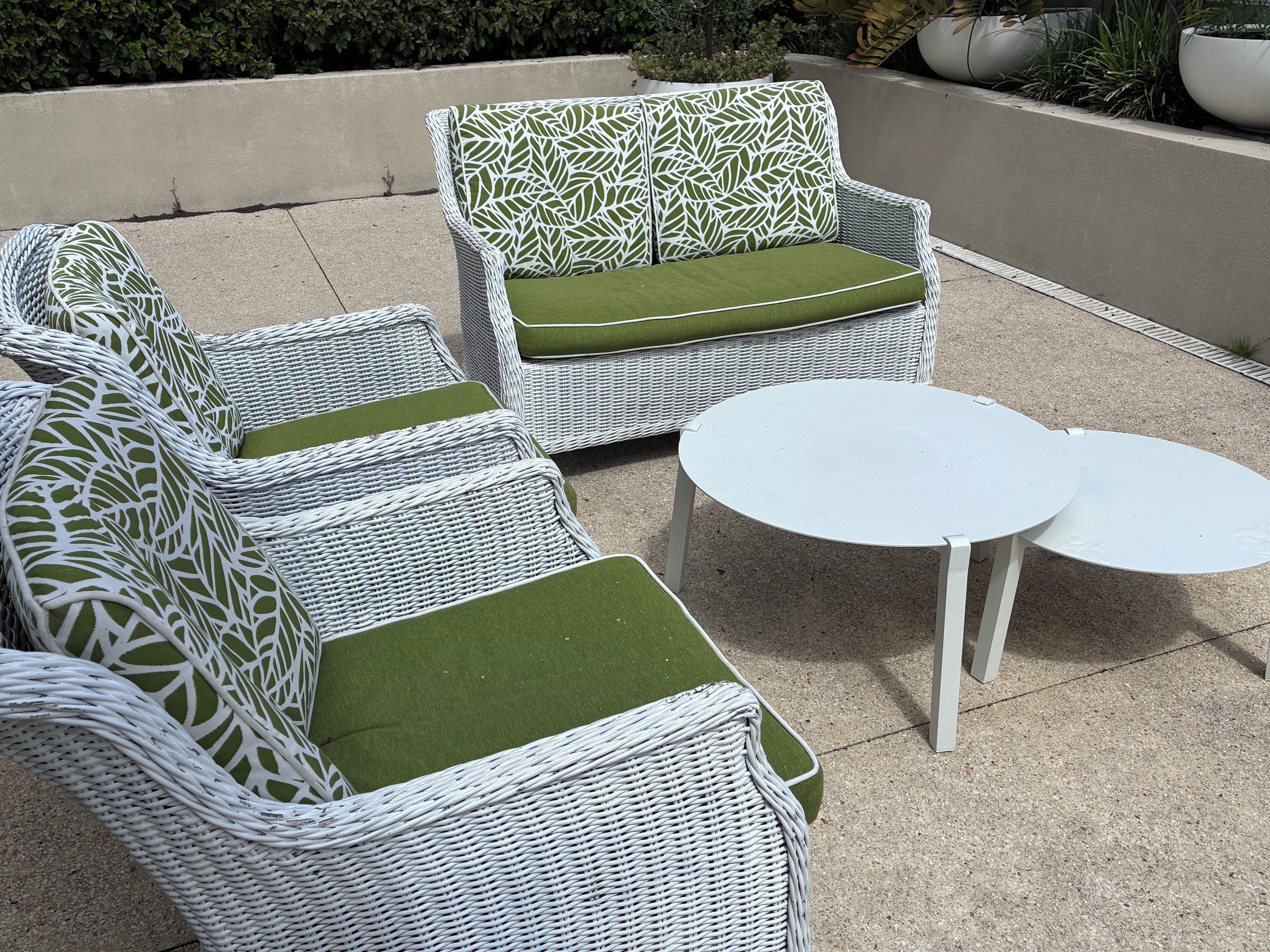 Outdoor wicker furniture with green cushions and two white round tables.