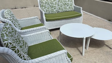 Outdoor wicker furniture with green cushions and two white round tables.