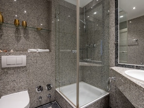Ein modernes Badezimmer mit einer gläsernen Dusche, einem weißen Waschbecken und einer Wand mit Marmorfliesen.