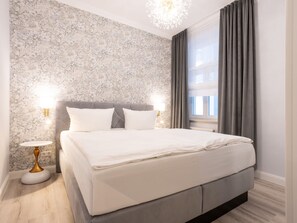Ein modernes Schlafzimmer mit einem großen Bett, einer Wand mit Marmoroptik, einem runden Nachttisch und einem Fenster mit Vorhängen.