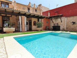 A swimming pool with a stone patio, a covered outdoor seating area, and a building with a red wall and stone facade. - Villa in Muro With Swimming Pool (Muro)