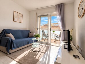Ett modernt vardagsrum med en soffa, ett soffbord i glas, en tv och en balkong med stolar och ett bord.