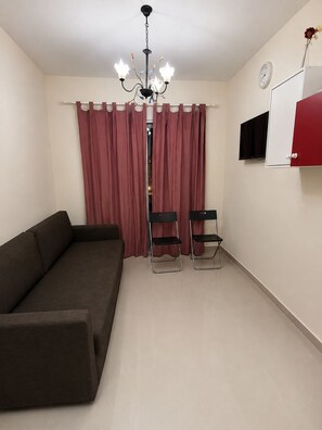 A room with a sofa, two chairs, a TV, a clock, and a red cabinet.