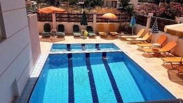 Una piscina rectangular con borde de azulejos, rodeada de sillas de descanso y sombrillas.